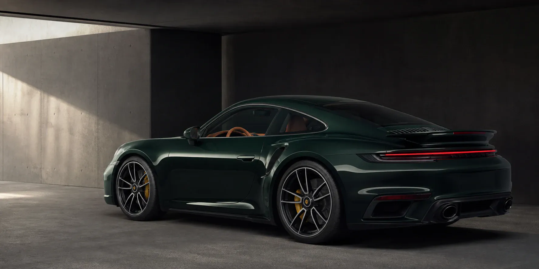 Editorial configuration study of a British Racing Green 992.2 Turbo S with a Terracotta cabin in a dark architectural garage.